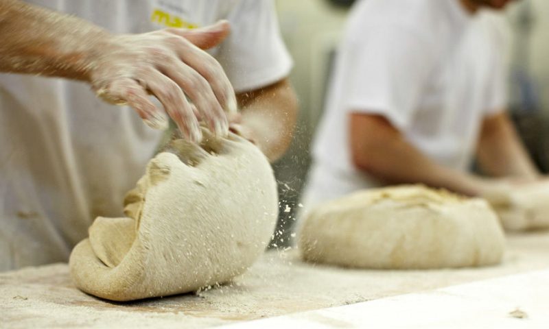 Ein Bäcker knetet den frischen Brotteig zur Zubereitung eines leckeren Brotes.
